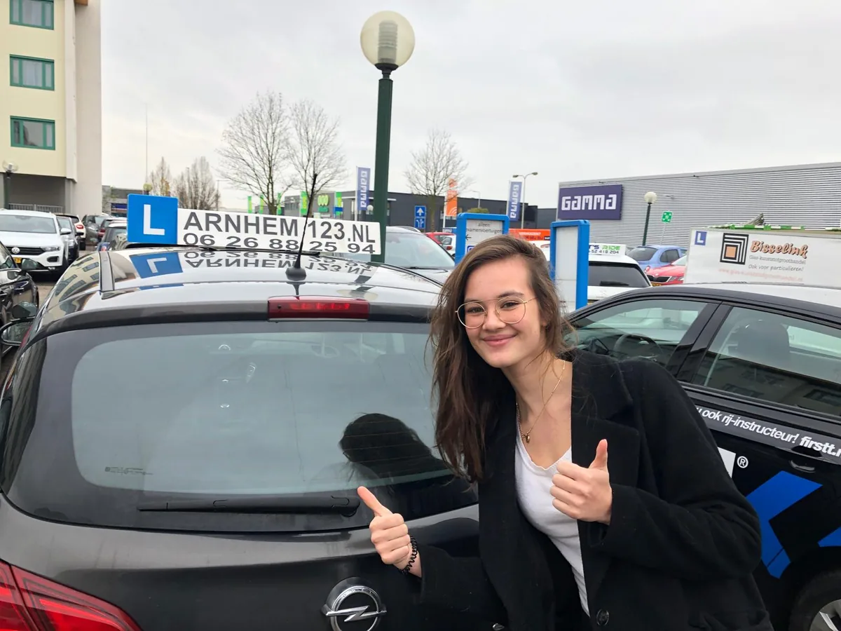 Leerling met twee duimen omhoog naast een lesauto van Rijschool Arnhem 123